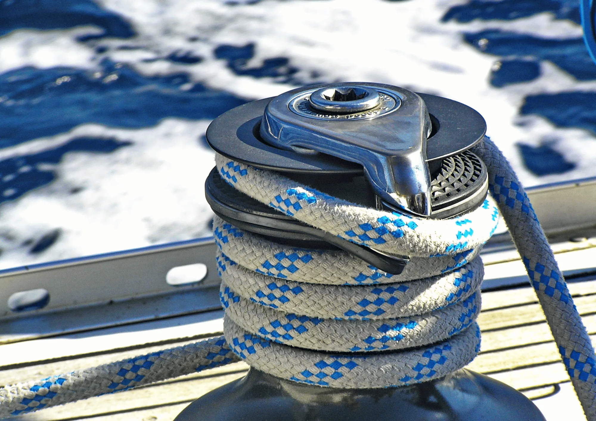 Sailboat winch wrapped with blue and white rope against the sea background.