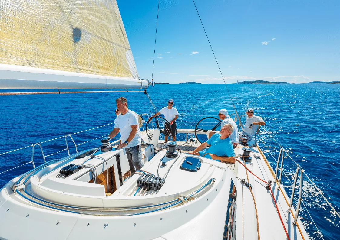 Crew sailing together on a yacht during a sunny offshore passage, blue ocean and islands in the background.