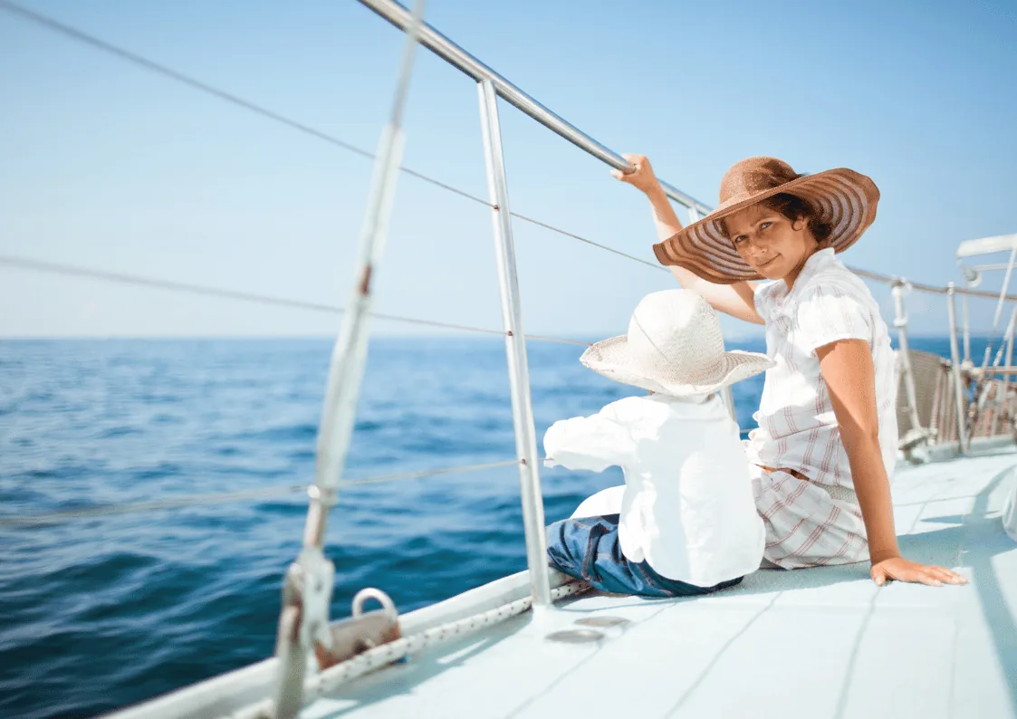 Child and parent sitting on the deck of a sailboat looking at the ocean on a sunny day.